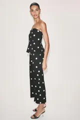 Mono largo de escote recto sin tirantes, con peplum en la cintura, perneras acampanadas y estampado de lunares.