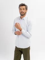 Camisa de vestir de manga larga en color celeste claro, con cuello clásico y cierre frontal de botones. Presenta un diseño de textura sutil y corte regular.