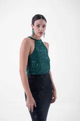 Vestido largo de fiesta con lentejuelas, compuesto por un top verde esmeralda con cuello halter y una falda negra ajustada con abertura lateral.