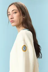 Cardigan de algodón color crudo, de corte corto y ajuste frontal con botones. Presenta detalles de ribetes a contraste en cuello, puños y ruedo, con una estética clásica y versátil.