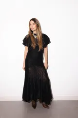 Vestido largo negro de encaje transparente con diseño geométrico, mangas cortas con volados y cuello alto.
