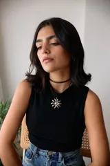 Collar con dije de acero quirúrgico en forma de flor tipo margarita, montado sobre un tiento de cuero negro.