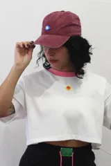 Gorra tipo baseball de color gris con efecto desgastado, presenta un detalle circular en color rosa y verde en la parte frontal.