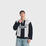 Sweater de punto con diseño de rayas verticales combinadas en azul marino y gris, cuello polo blanco con ribete oscuro y cierre frontal parcial. Cuenta con inscripciones gráficas bordadas en el pecho.