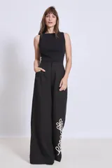 Pantalón negro de corte palazzo con bolsillos laterales y apliques bordados de hojas en color crudo en una pierna.