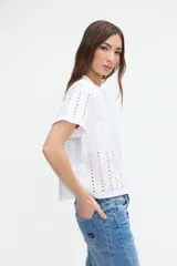 Blusa corta de broderie blanca, de manga corta, con cuello redondo y cierre frontal de botones.