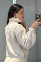 Buzo de chenille color blanco, con cuello alto tipo polera, mangas largas con puños ajustados y diseño de tejido acanalado.