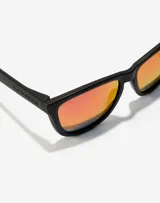 Lentes de sol Hawkers modelo One, con armazón negro mate y cristales polarizados con efecto espejado en tono rojizo.