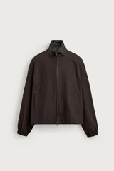 Cazadora relaxed fit de color marrón oscuro confeccionada en tejido de algodón. Presenta cuello subido de piel, manga larga con puño elástico, bolsillos de vivo en la cadera y cierre frontal con cremallera.