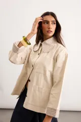Sobrecamisa de algodón color beige, de corte holgado, con bolsillos frontales aplicados, cuello camisero y puños en contraste con estampado de cuadros en tonos verde oscuro. Cuenta con cierre frontal de botones metálicos.