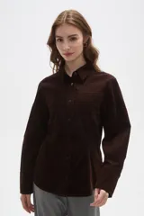 Camisa de pana color marrón, con cuello camisero, cierre frontal de botones y bolsillos en el pecho. Presenta un corte entallado y mangas largas.