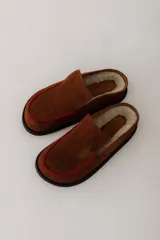 Zueco de cuero color marrón oscuro, con costuras decorativas en hilo rojo en el empeine y suela plana de goma.