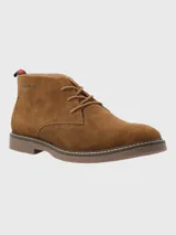 Bota tipo chukka de Hush Puppies, confeccionada en descarne color marrón, con cordones al tono, suela de goma y detalle de tirador en el talón con franjas rojas y negras.