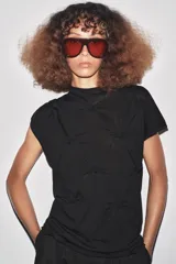 Top negro de manga corta y cuello subido, con detalle de nudos y frunces distribuidos en el frente y laterales, creando textura.