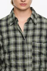 Camisa de corte recto y largo medio, confeccionada en tejido de algodón con textura. Presenta un diseño de cuadros en tonos rojo, negro y azul, cuello camisero, cierre frontal con botones, manga larga con puños abotonados y bolsillo de plastrón en el pecho.