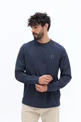 Remera de manga larga color blanco roto o gris muy claro, con escote redondo y un pequeño logo circular estampado en el pecho.