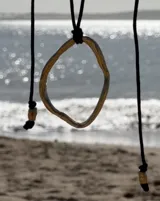 Collar con dije colgante de forma orgánica e irregular, acabado dorado, suspendido de un cordón negro de algodón natural.