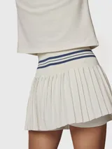Falda tipo skort con diseño plisado, confeccionada en tejido técnico de secado rápido. Presenta una cintura alta elástica con detalle de rayas horizontales en color azul marino y short integrado con bolsillo.