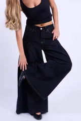 Jean de corte wide leg en color negro, con diseño de costuras curvas en la parte superior y pinzas que aportan volumen a la prenda. Presenta tiro medio, cierre frontal con botón y costuras en contraste.