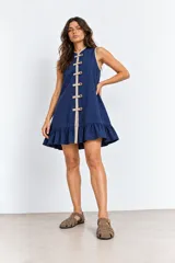 Vestido corto azul marino sin mangas, con cuello mao y cierre frontal de alamares decorativos en tono beige. Presenta ribetes en contraste y un delicado volado en el ruedo.