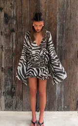 Vestido corto con estampado animal print tipo zebra, escote en V cruzado, mangas largas amplias y detalle de volados en la parte inferior.