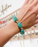 Pulsera elástica compuesta por piedras de resina en tono verde agua, intercaladas con piezas metálicas doradas.