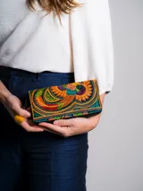 Billetera de tela bordada con diseño de ave multicolor. Tiene cierre de cremallera y tirador con pompón amarillo.