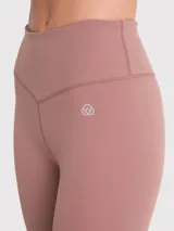 Calza deportiva de tiro alto con largo hasta el tobillo, confeccionada en tejido elástico de color tierra. Presenta un diseño liso sin bolsillos con costuras reforzadas y logo pequeño en la cadera.