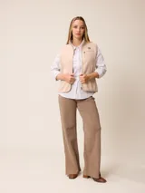 Chaleco de sherpa color beige con cierre frontal completo, cuello alto y bolsillo con cierre en el pecho que incluye un detalle circular con logo.