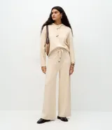 Buzo de punto color beige con capucha y cordones largos con punteras metálicas, de corte regular y mangas largas.