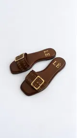 Sandalias planas color tostado, con una tira ancha en el empeine decorada con ojalillos metálicos y una hebilla grande central.