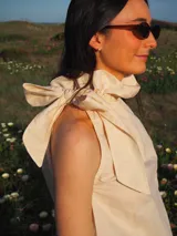 Blusa de lino sin mangas, con cuello alto fruncido y un lazo decorativo al costado. Diseño a rayas finas en tonos amarillo manteca y blanco, con corte recto y ligero.