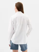 Camisa blanca de manga larga con cuello clásico, cierre de botones frontales y un bolsillo en el pecho.