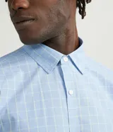 Camisa de manga larga con estampado cuadrillé en tonos celestes y blancos, confeccionada en tejido plano de algodón. Presenta cuello solapa y cierre frontal con botones.