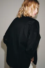 Camisa de cuello redondo y manga corta abullonada, color negro, de corte recto con aberturas laterales y cierre frontal con botones. Perteneciente a la colección ZARA Woman Collection.