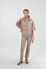 Camisa de cuero ovino color rosa pálido, de corte recto y estilo minimalista. Tiene mangas cortas, cuello clásico, cierre con botones a presión plateados y bolsillos delanteros con solapa.