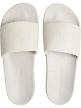 Ojotas tipo slide blancas, con tira ancha de lona que presenta el logo 'CK' en relieve y la inscripción 'CALVIN KLEIN JEANS' grabada en la plantilla ergonómica.