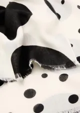 Pañuelo fluido de poliéster color blanco con estampado de lunares negros y grises, con terminaciones deshilachadas.