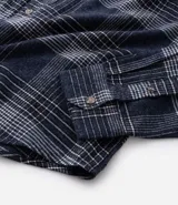 Camisa de manga larga confeccionada en franela de algodón, con cuello bowling y cierre frontal de botones. Presenta un diseño de estampado a cuadros en tonos azul marino y gris, con un corte regular.