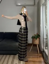 Pantalón tipo palazo de corte amplio y tiro alto, confeccionado en tela con estampado de cuadros escoceses en tonos marrones, blancos y negros. Cuenta con cintura elástica y bolsillos laterales.