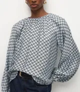 Blusa de mangas largas abullonadas con cuello redondo fruncido y diseño de estampa geométrica en tonos azul y blanco.