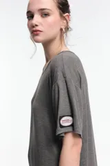 Vestido midi color beige, de corte oversized, con cuello redondo, manga corta y tajos laterales. Presenta un parche decorativo en la manga.