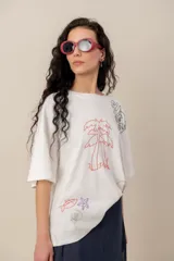 Remera blanca de manga corta y corte oversize, con bordados de motivos tropicales y marinos como palmeras, peces, estrella de mar y caracol.