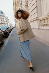 Chaqueta de corte recto y estilo camisero en color beige, con cuello solapa, manga larga y cierre frontal con botones. Presenta dos bolsillos delanteros de plastrón.