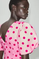 Top rosado con estampado de lunares fucsia, de cuello redondo y mangas cortas abullonadas con pliegues. Cuenta con escote en V en la espalda y cierre con cremallera oculta.