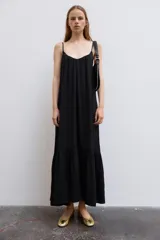 Vestido midi de color negro, confeccionado en tejido fluido, con escote en V y tirantes finos ajustables. Presenta frunces en el pecho y un volante en el bajo.