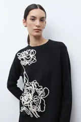 Sweater de punto color rojo melange, con cuello redondo, manga larga y detalle de bordado floral en relieve en color crudo en el frente.