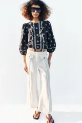 Blusa azul marino con estampado de lunares blancos, cuello redondo y mangas abullonadas. Presenta detalles de bordados perforados, volantes delanteros y acabados elásticos.