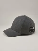 Gorra de béisbol de paño en color gris oscuro, con visera curva y parche rectangular negro con logo de la marca en el lateral.