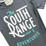 Remera gris oscuro de algodón con estampa frontal en blanco y turquesa que dice 'The South Range Adventures'.